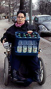 Frau im Rollstuhl transportiert einen Kasten Mineralwasser